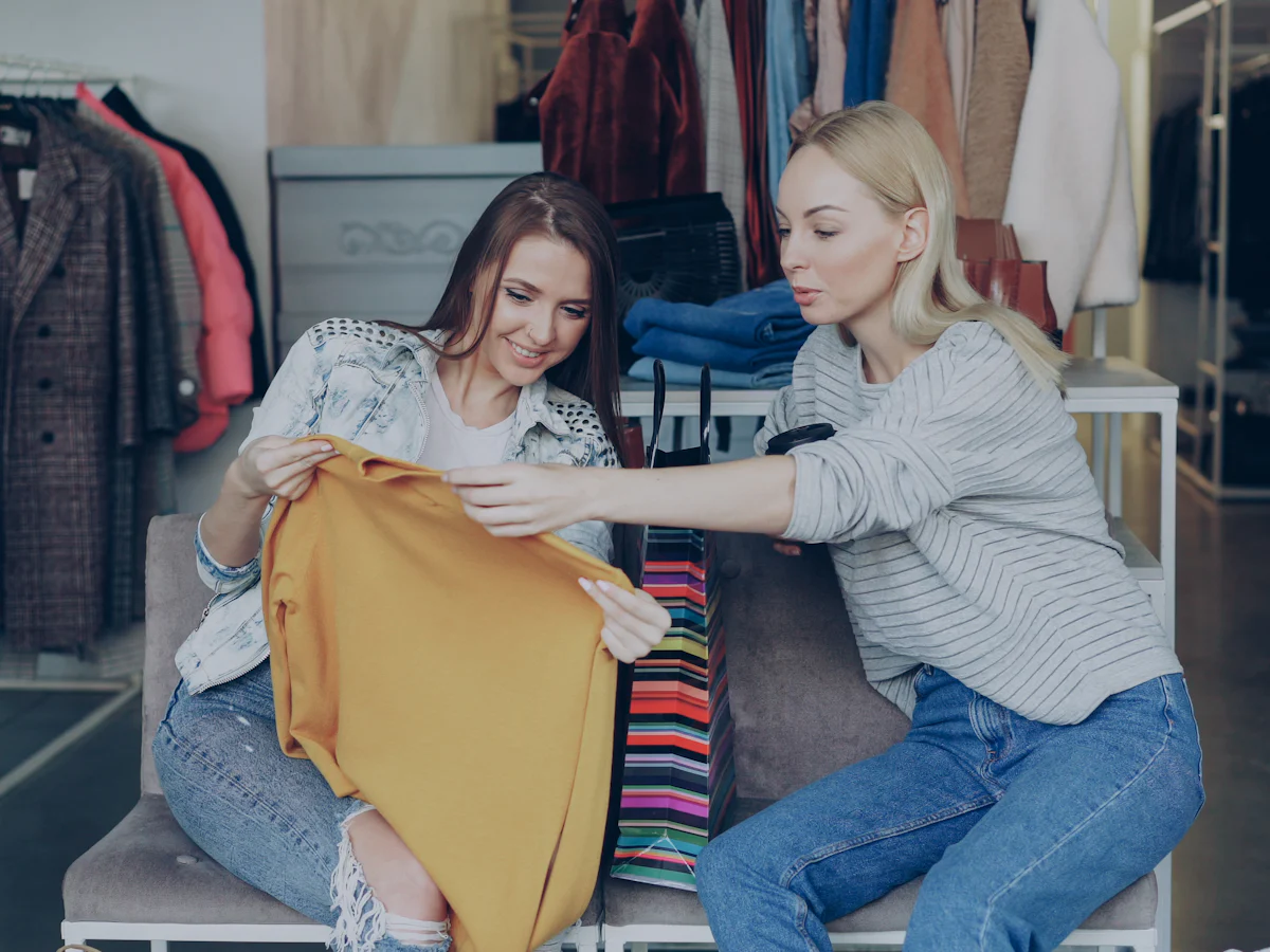 Two women talking over a jumper in a small clothing store